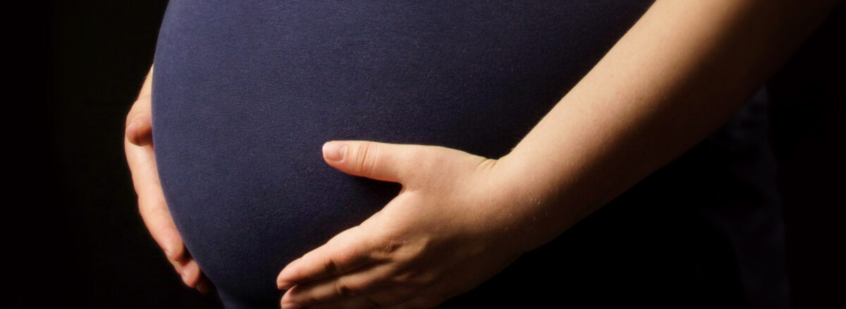 Pregnant woman holding hands over belly on black background